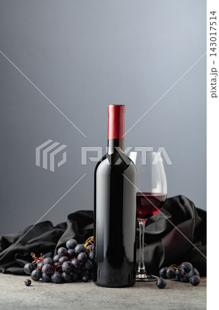 Bottle of red wine with grapes on a grey background. Bottle of red wine with grapes on a grey background. 143017514