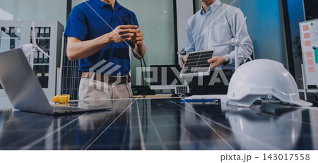 Two Asian engineers wearing hardhats and safety vests discussing solar panel installation and renewable energy project in the office. Two Asian engineers wearing hardhats and safety vests discussing solar panel installation and renewable energy project in the office. 143017558