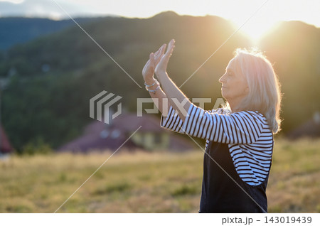 Senior woman practicing meditation outdoors in peaceful countryside. 143019439