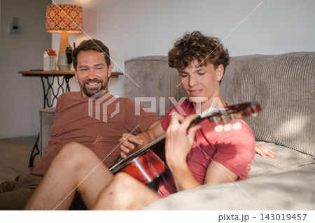 Father teaching teenage son to play guitar at home. 143019457