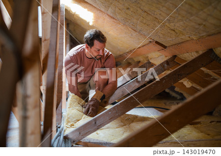 Homeowner insulating attic during home renovation project. Homeowner insulating attic during home renovation project. 143019470
