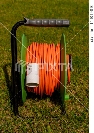 Orange extension cord reel on green grass in garden 143019810