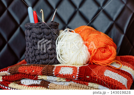 Handmade crochet blanket with yarn balls and hooks. Crochet hobby for mental wellbeing, digital detox Handmade crochet blanket with yarn balls and hooks. Crochet hobby for mental wellbeing, digital detox 143019828