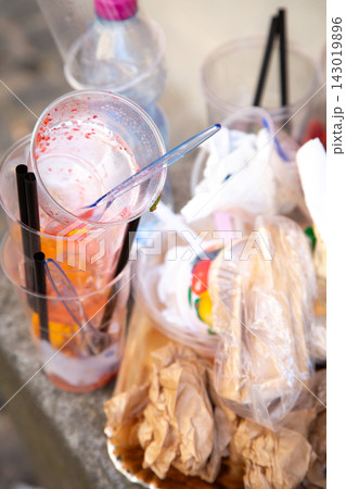 Discarded disposable cups, straws, crumpled paper, and food packaging scattered together on stone surface after outdoor gathering, highlighting messy cleanup, waste, and litter Discarded disposable cups, straws, crumpled paper, and food packaging scattered together on stone surface after outdoor gathering, highlighting messy cleanup, waste, and litter 143019896