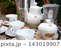 White porcelain tea set with floral pattern on mosaic table beside cups, sugar bowl, teapot, and metal coffee pot in soft natural light, with porcelain, teaset, teapot, cup detail 143019907