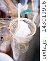 Used plastic dessert cup with spoon and crumpled tissue, showing leftover cream and stains inside clear container, with blurred takeaway cups in background, close-up vertical food waste scene 143019916