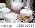White porcelain tea set with floral pattern on mosaic table beside cups, sugar bowl, teapot, and metal coffee pot in soft natural light, with porcelain, teaset, teapot, cup detail 143019918
