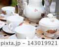 Floral porcelain teacups and matching teapot beside metal kettle on mosaic table, arranged outdoors with soft natural light, calm breakfast setting, ceramic drinkware, vintage charm 143019921