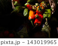 Colorful hot chili peppers piled together with green, orange, and red ripening pods in moody low light, showing fresh harvested produce with textured skins and stems 143019965