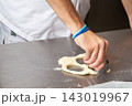 Close up of hand cutting rolled dough with round metal cutter on stainless steel counter in bright kitchen, showing pastry preparation, baking work, simple ingredients, and focused manual food craft 143019967