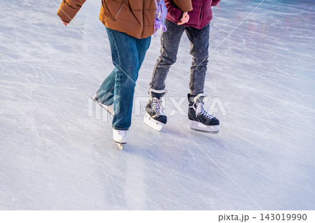 Two People Ice Skating Together on Winter Rink. Cropped view of two people skating together across outdoor ice rink. Ice skates, casual winter clothing, frozen surface illustrate seasonal recreation Two People Ice Skating Together on Winter Rink. Cropped view of two people skating together across outdoor ice rink. Ice skates, casual winter clothing, frozen surface illustrate seasonal recreation 143019990