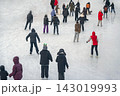 Crowded Outdoor Ice Rink Viewed From Above. High-angle view, numerous people skating across broad winter ice rink. Busy public recreation, seasonal activity, urban leisure. Winter sport background 143019993