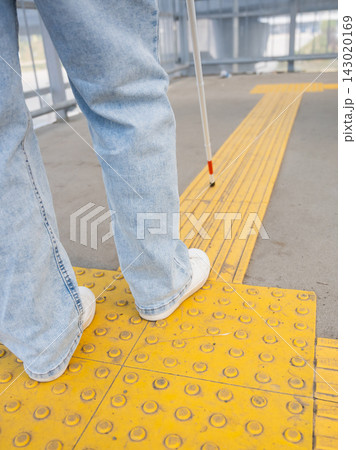 A blind woman walks using a cane and tactile tiles. 143020169