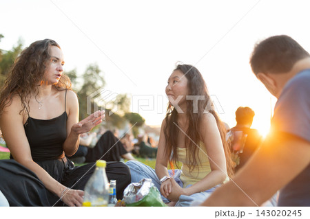 Friends gather in a park during sunset to chat and enjoy snacks together on a warm evening 143020245