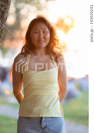 Young asian woman smiling outdoors during golden hour sunset 143020281