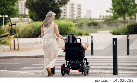 Caregiver pushing adult with spina bifida in wheelchair 143020282