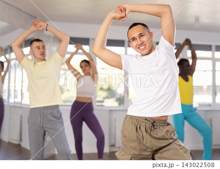 Happy multinational young man and woman dancing and training latin dance movements in ballroom together 143022508