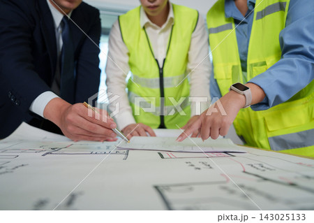 Engineers and architect reviewing floor plan blueprints on table for construction project 143025133