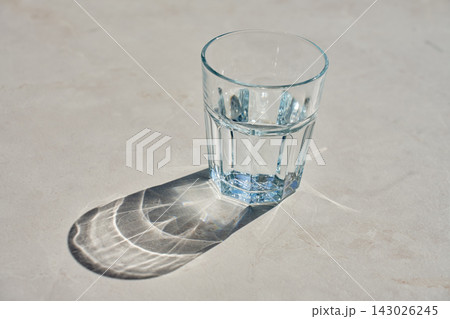 Glass of water in sunlight with reflections and shadows on table 143026245