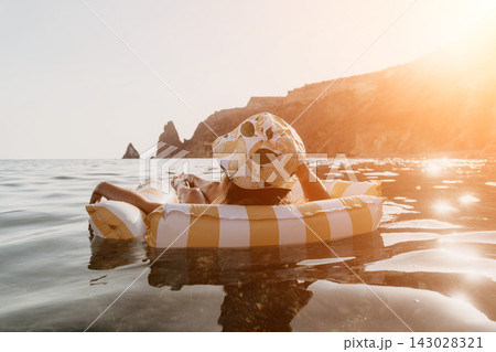 Woman, Inflatable, Beach: A woman relaxes on a striped inflatable raft in the ocean, with rocky cliffs in the background. Woman, Inflatable, Beach: A woman relaxes on a striped inflatable raft in the ocean, with rocky cliffs in the background. 143028321
