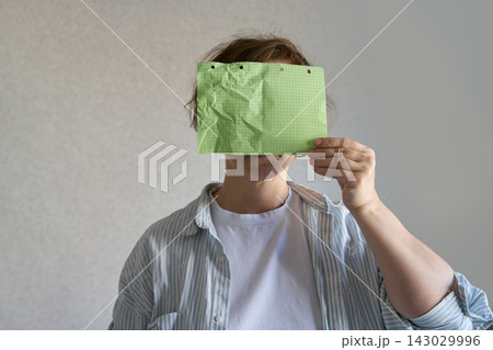 Crumpled Green Squared Sheet Held Across Face By Woman In Open Striped Shirt, With Bent Paper Edges Crumpled Green Squared Sheet Held Across Face By Woman In Open Striped Shirt, With Bent Paper Edges 143029996