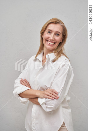 Blonde Woman Standing With Arms Crossed And Smiling In White Shirt Against Plain Gray Studio Blonde Woman Standing With Arms Crossed And Smiling In White Shirt Against Plain Gray Studio 143030035