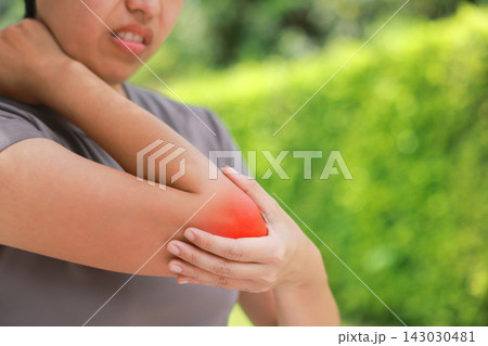 Close up unhappy Asian woman touching her elbow with a red highlighted area indicating severe joint pain, arthritis, muscle ache or sports injury. Healthcare, physical therapy, and medical concept. 143030481