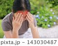 Stressed young Asian woman sitting outdoors touching her head with red highlighted area indicating severe headache, migraine, or brain pain. Concept of sickness, healthcare, tension and mental health. 143030487