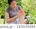 Stressed young Asian woman sitting on a chair touching her bare knee with red highlighted area indicating severe joint pain, arthritis, muscle ache or sports injury. Healthcare, medical concept. 143030489