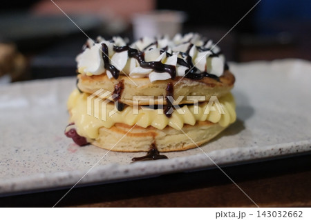 Stack of fluffy pancakes topped with whipped cream and chocolate sauce 143032662