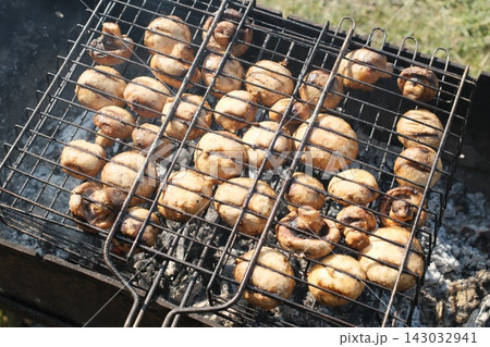 Fresh mushrooms cooking on a metal grill over hot charcoal outdoors Fresh mushrooms cooking on a metal grill over hot charcoal outdoors 143032941