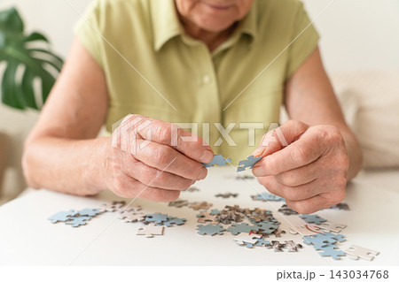 Senior woman's hands assembling puzzle pieces, engaging in mental exercise and brain training for dementia prevention 143034768