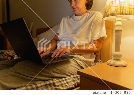 Caucasian adult female working on laptop in bed near lamp at night Caucasian adult female working on laptop in bed near lamp at night 143034959