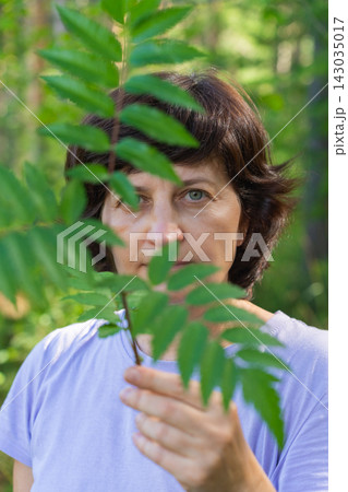 Mature caucasian female partially obscured by leaf in forest setting 143035017