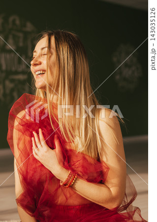 Woman with closed eyes with blond long hair and a red transparent cloth in her hands, portrait 143035126