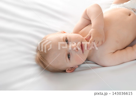 Happy naked baby in diaper lying on his back on the white sheet and touching his face. Baby girl with red hair looking at camera. Light background. Little child. Serious emotion. Advertising Mockup Happy naked baby in diaper lying on his back on the white sheet and touching his face. Baby girl with red hair looking at camera. Light background. Little child. Serious emotion. Advertising Mockup 143036615