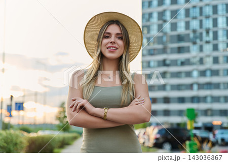 Confident young woman in straw hat standing with arms crossed outdoors Confident young woman in straw hat standing with arms crossed outdoors 143036867