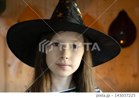 Halloween. Sad pensive girl in witch costume celebrating Halloween. Copy space. Portrait of unhappy little girl wearing Halloween hat masquerade as a witch 143037225