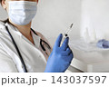 Nurse pushing air out of syringe for vaccine injection. Doctor wearing blue gloves and medical mask. Person holds a syringe with medicine in his hand Close Up. She ready to give an injection. Science 143037597