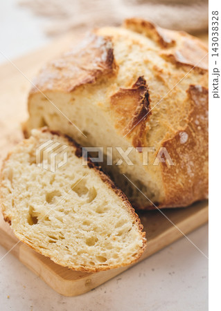Sliced artisan sourdough bread with airy crumb on wooden board, glass of milk, and knitted cloth. Ideal for culinary, baking, and food photography projects. Sliced artisan sourdough bread with airy crumb on wooden board, glass of milk, and knitted cloth. Ideal for culinary, baking, and food photography projects. 143038328