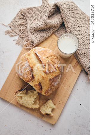 Sliced artisan sourdough bread with airy crumb on wooden board, glass of milk, and knitted cloth. Ideal for culinary, baking, and food photography projects. Sliced artisan sourdough bread with airy crumb on wooden board, glass of milk, and knitted cloth. Ideal for culinary, baking, and food photography projects. 143038714