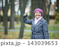 Woman waves while standing among trees at a park during autumn season in daylight 143039653