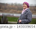 Woman stands outdoors near water with a smile and a beret during a cloudy day in autumn 143039654