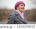 Woman wears a pink beret and scarf while standing outdoors on a cloudy day in a park 143039655