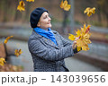Woman enjoys autumn leaves in a park on a cool day while smiling and tossing leaves in the air 143039656