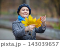 Woman holds large yellow leaves in a park, enjoying the autumn season with a smile and blue scarf 143039657