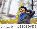 Woman smiles and poses in front of a large decorative star with lights during a winter event in a city setting 143039658
