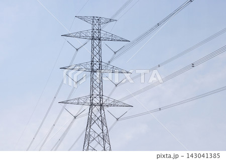 A high voltage electrical power pylon tower standing strong under a clear soft blue sky, supporting long distance transmission cables. High Quality Photo A high voltage electrical power pylon tower standing strong under a clear soft blue sky, supporting long distance transmission cables. High Quality Photo 143041385