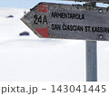 Weathered wooden directional trail sign numbered 24A pointing toward Armentarola and San Ciascian St Kassian in a snowy alpine landscape. 143041445