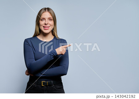 Young woman pointing index finger to copy space on gray background 143042192